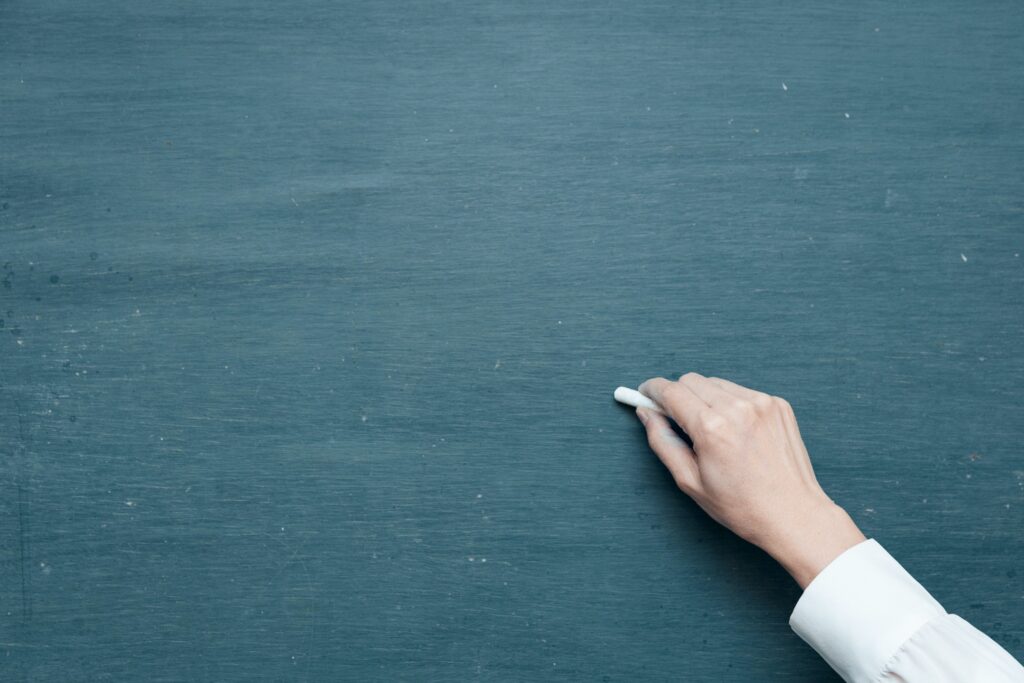 A photo of a hand holding a piece of chalk against a blank blackboard