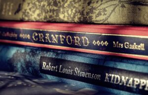 Cropped close-up on a pile of worn hardback copies of Robert Louis Stevenson's Kidnapped and Elizabeth Gaskell's Cranford in jewel tones