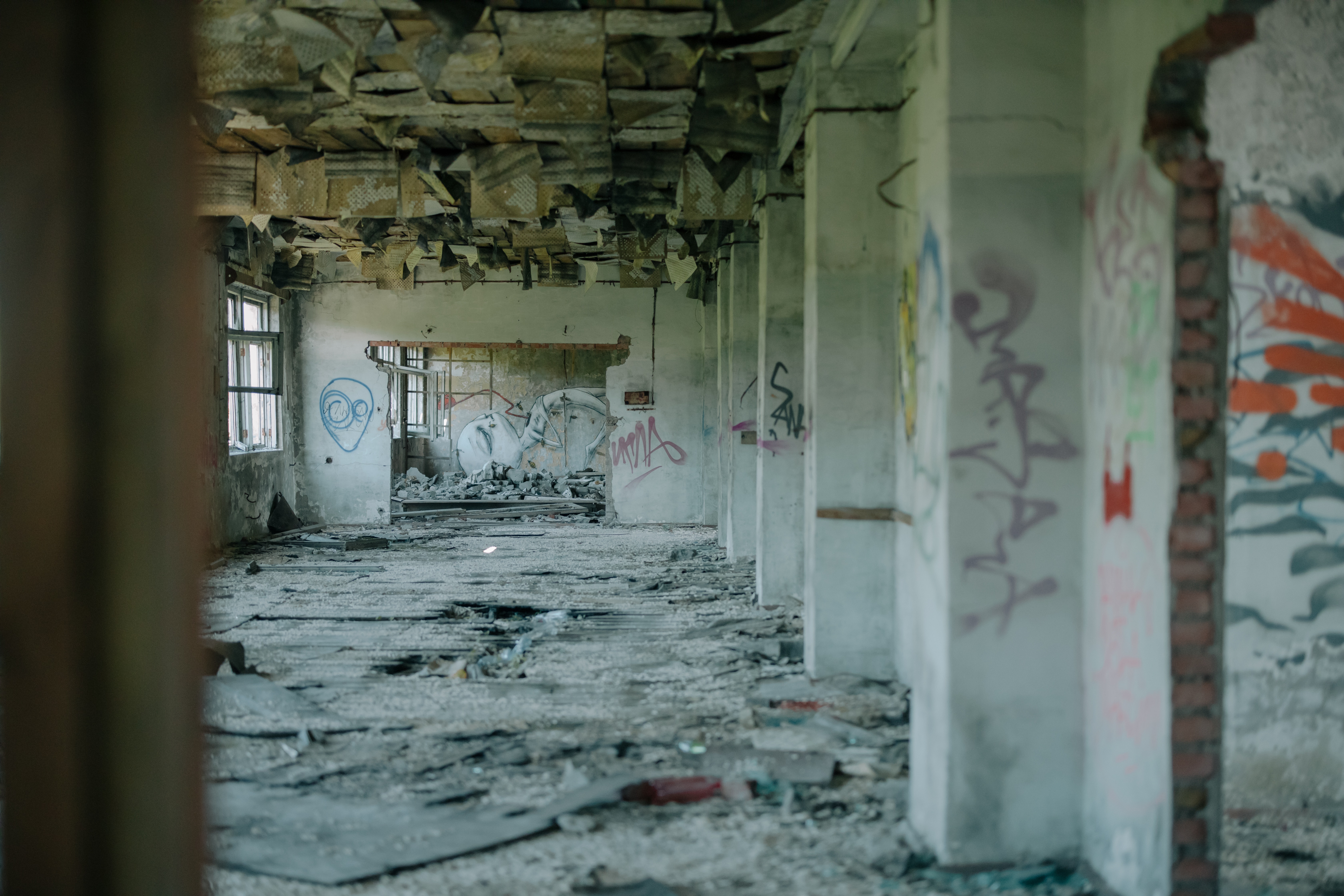 Image of the interior of an abandoned building. Lots of concrete, graffiti and collapsed roof tiles